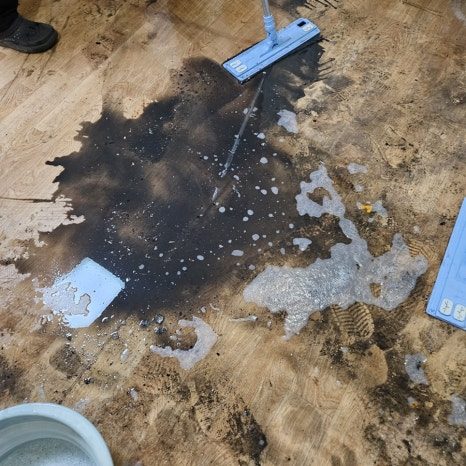 밀대로 검은 오염을 닦아내는 중, 흰 거품과 물기가 바닥에 퍼져 있다